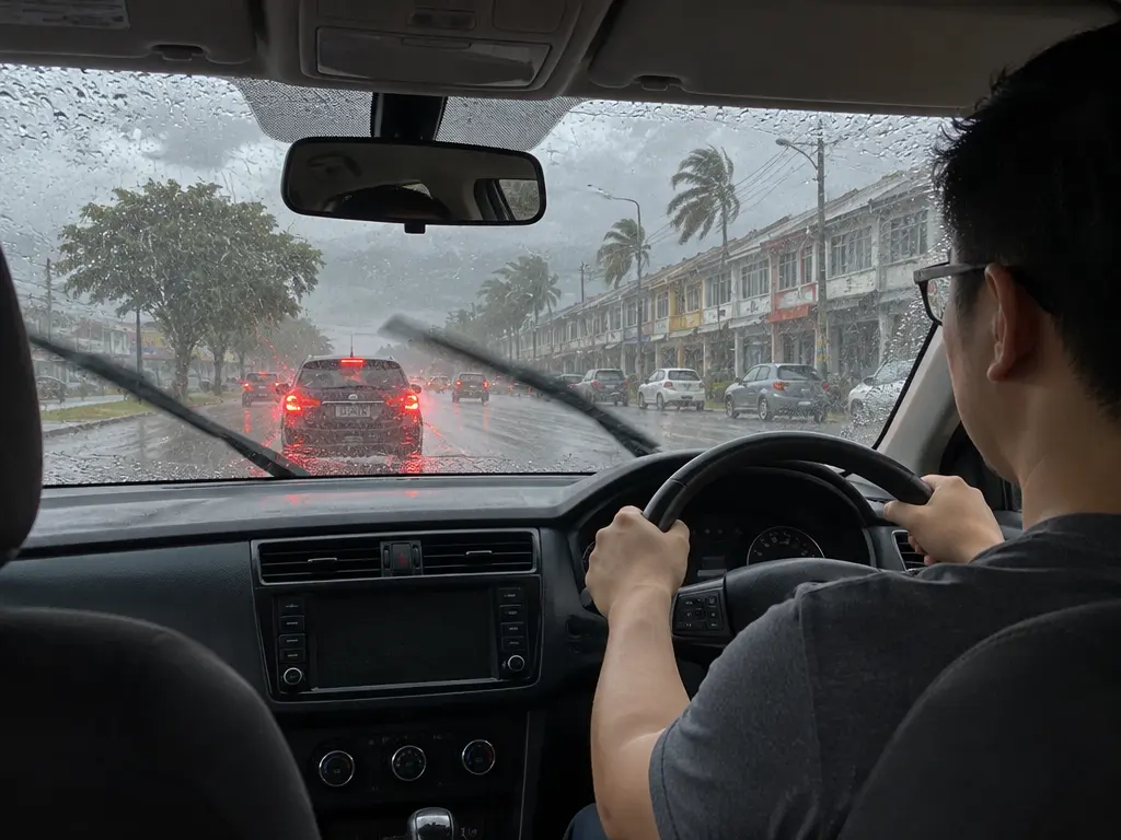 示意图:大雨中司机双手握方向盘慢驾,雨刷刮着挡风玻璃
